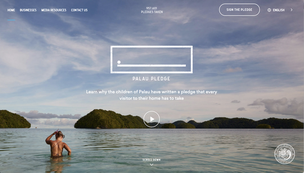 The image is a screenshot of a website titled "Palau Pledge." The header includes navigation links: "HOME," "BUSINESSES," "MEDIA RESOURCES," and "CONTACT US." The page features a scenic background of a person standing in the water, looking towards distant islands under a partly cloudy sky. The main content area contains the Palau Pledge logo and a text overlay that reads, "Learn why the children of Palau have written a pledge that every visitor to their home has to take." There is also a play button for a video and an option to "SIGN THE PLEDGE." In the bottom right corner, there is a seal that likely represents the Palau Pledge or an associated organization.