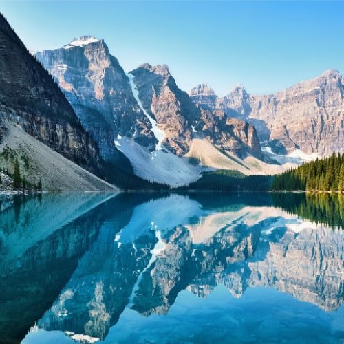 A serene view of a mountain lake surrounded by towering peaks and lush green forests, with the clear blue sky reflecting perfectly on the still waters. The image evokes a sense of tranquility and natural beauty, capturing the pristine landscape in vivid detail.