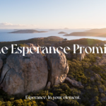 A scenic aerial view of Esperance, Australia, featuring rugged rock formations, lush green vegetation, and the deep blue ocean stretching toward the horizon. The golden light of the setting sun casts a warm glow over the landscape. White text in the center reads, "The Esperance Promise," with a tagline below stating, "Esperance. In your element."