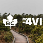 A scenic wooden boardwalk winds through lush green vegetation in a natural setting, with the logos of BC (British Columbia) and 4VI prominently displayed in the foreground. The sky is overcast, creating a serene and tranquil atmosphere.