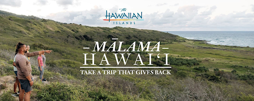 A group of people stands on a lush coastal hillside in Hawaiʻi, looking out over the ocean. One person points toward the horizon. The image promotes the Mālama Hawaiʻi initiative with the slogan "Take a Trip That Gives Back."
