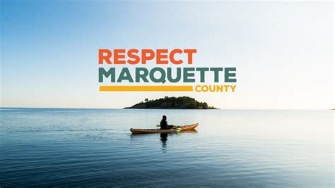 A scenic shot of a kayaker on the water in Marquette County, featuring a distant island and text overlay 'RESPECT MARQUETTE COUNTY'.
