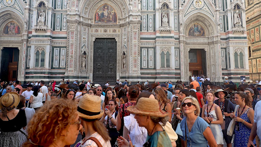 A large crowd of tourists gathers in front of the ornate entrance of the Florence Cathedral (Duomo di Firenze) in Italy, showcasing the challenges of overtourism at popular heritage sites.