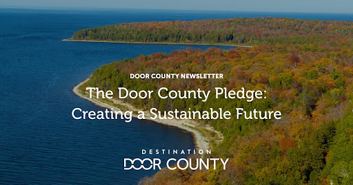 Aerial view of a forested shoreline in Door County, Wisconsin, with calm blue water and autumn foliage, overlaid with the text “The Door County Pledge: Creating a Sustainable Future.”