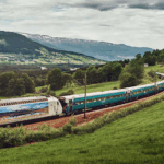 Scenic train traveling through green countryside near Bergen, Norway, with mountains and farmland in the background.